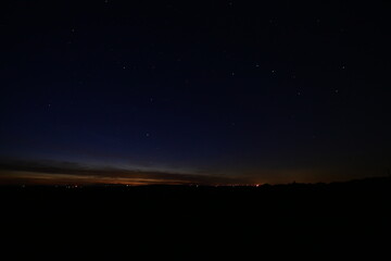 Fototapeta premium A breathtaking view of the night sky above a brightly lit city, featuring countless stars and distant Starlink satellites.