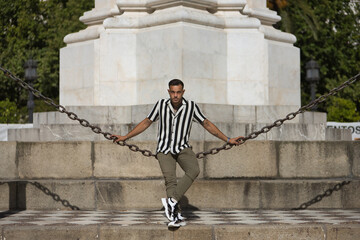 Young, brunette, Hispanic, modern man, wearing crochet shirt with black and white stripes and...