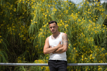 Young, brunette, Hispanic, modern man in white tank top and jeans, with a serious and defiant look,...