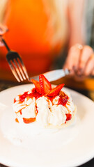 A woman cutting a beautiful slice of pavlova with strawberries and whipped cream. Blurred background, focus on the dessert. Perfect for baking, celebrations, and gourmet dessert concepts.