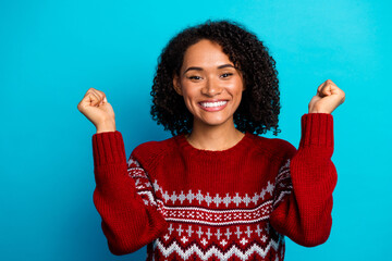 Funny bright young woman in red christmas sweater celebrates joy with big smile against blue background and holiday sparkle vibe today