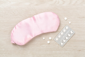 Sleeping mask with pills on wooden background, top view