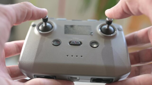 Close-up of hands operating a drone remote controller, pressing buttons and moving joysticks with realistic clicking and beeping sounds in bright indoor light