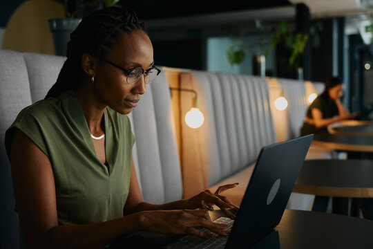 Focused young black businesswoman typing on laptop sitting at desk in office lounge