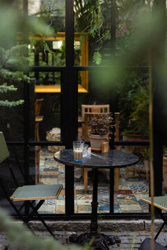 patio table and chairs tucked away in a cozy, leafy indoor outdoor cafe with mirror doors and lots of green and tile floors in europe
