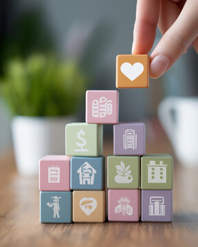 A businesswoman&rsquo;s hand stacking pastel blocks with icons for salary, health care, pension, and paid leave in cozy home office