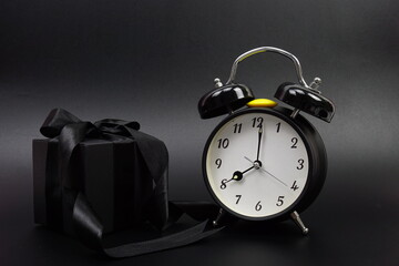Gift boxes presents with black ribbon and alarm clock on black background
