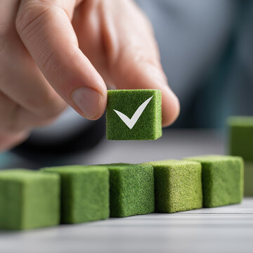 Executive hand arranging green checkmark cube representing corporate responsibility, compliance, and quality assurance in office environment- 