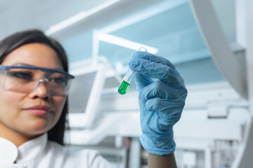 Woman lab researcher in protective gear, safety glasses and blue gloves carefully pipetting yellow...