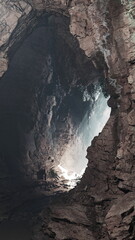 Sunbeams filter through the entrance of a stone cave, highlighting rocky textures.