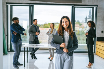 Business woman smiling, holding clipboard, diverse team in background