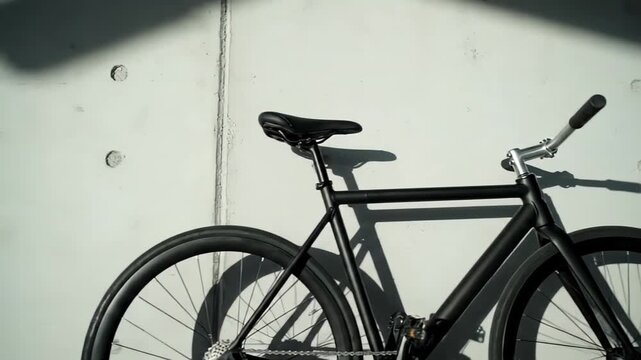 Contemporary black single speed bike propped up next to a concrete city wall. Strong shadows are cast by the sunlight on a bright day in the urban setting