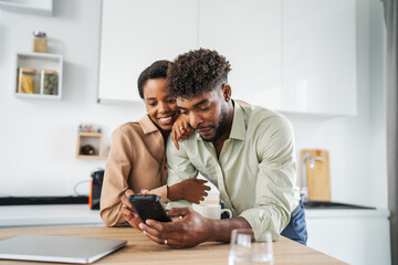 Young black couple sharing content on smart phone in kitchen