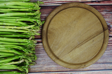 Bunch of fresh green asparagus stems with cutting wooden board on wooden background