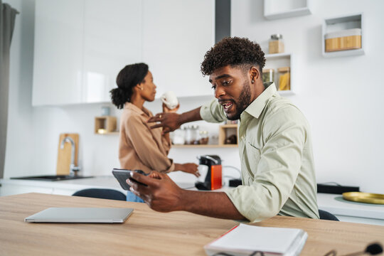 Young black couple multitasking and communicating in modern kitchen