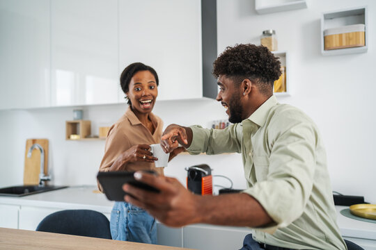 Diverse couple enjoying morning coffee laughing with tablet