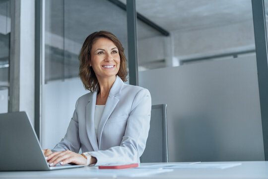 Mature professional it specialist latin hispanic business lady working on laptop pc sitting at desk in modern office space. 40s middle-aged European woman using computer technology app for work online