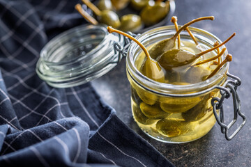 Pickled capers berries in jar on black table.