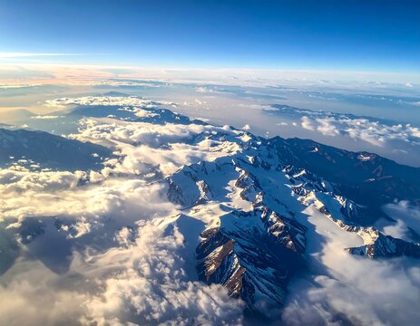Aerial view of snow-capped mountain range piercing through fluffy clouds, with a blue sky above and other lower ranges