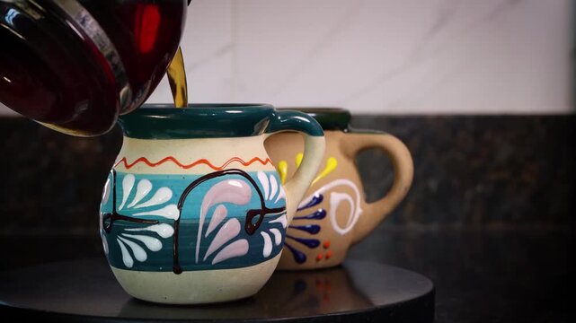 Hot black coffee being poured from a glass pot into a colorful, handmade ceramic mug in a kitchen. mexican coffee