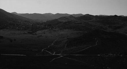 Mountain valley with winding roads in black and white. Black and white landscape of mountain valley with winding roads, small town, and distant peaks, evoking mood of isolation and depth.