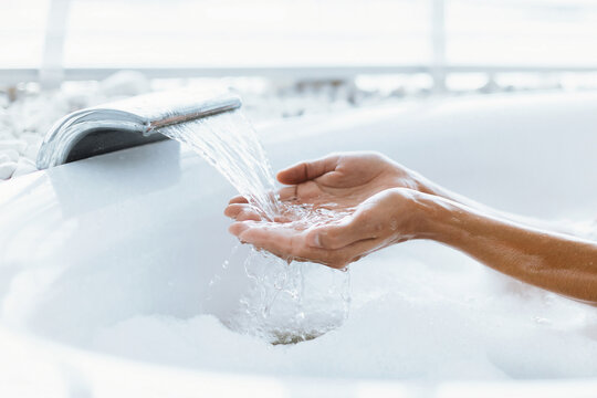 Hands cupped under a soothing stream of water flowing from a modern fixture. The warm setting features bubbles and a tranquil atmosphere, perfect for self-care and relaxation. - Powered by Adobe