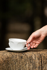 close up of hand holding white ceramic coffee cup on rustic wooden surface outdoors