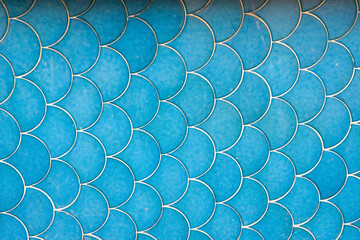 A vibrant, close-up pattern of bright turquoise blue fish scale or scallop-shaped ceramic tiles with white grout, creating a detailed background texture.