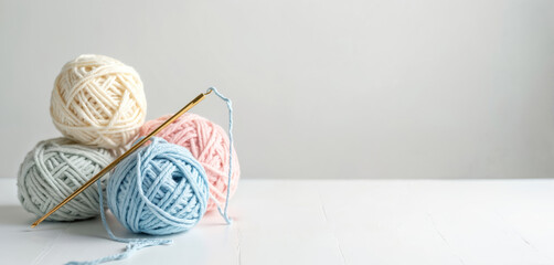 Pastel colored cotton yarn balls and crochet hook on white table. Soft blue, pink, beige and grey yarn for handmade crafts. Crochet tool for needlework hobby on clean background.