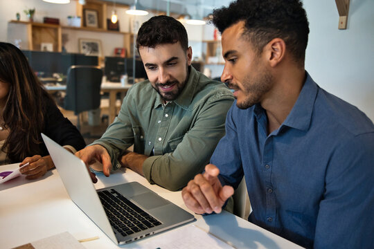 Two young multiracial coworkers collaborating on a laptop while developing a creative project in a modern office environment. Teamwork, innovation and startup culture concept - Powered by Adobe