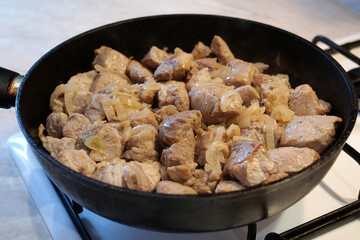 Frying meat. Pieces of meat with onion in frying pan on gas stove