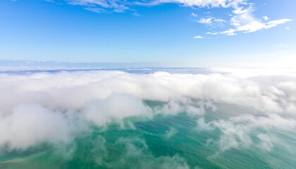 Obraz premium An aerial view capturing fluffy white clouds rolling over turquoise ocean water under a bright, clear, blue sky with soft haze