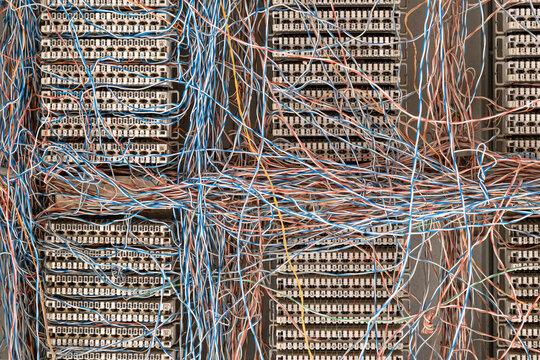 network hub, multi-colored copper wires crossing over white numbered cross-connect panels. The chaotic a a large old telephone telecommunications network. - Powered by Adobe
