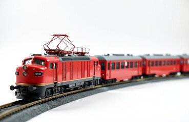 Red electric train model on display track. Miniature locomotive pulls passenger cars on white background studio. Small railway vehicle with detailed design.