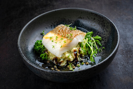 Fried nordic skrei cod white sea fish filet with mashed potatoes, green vegetable and balsamic vinegar relish umami sauce