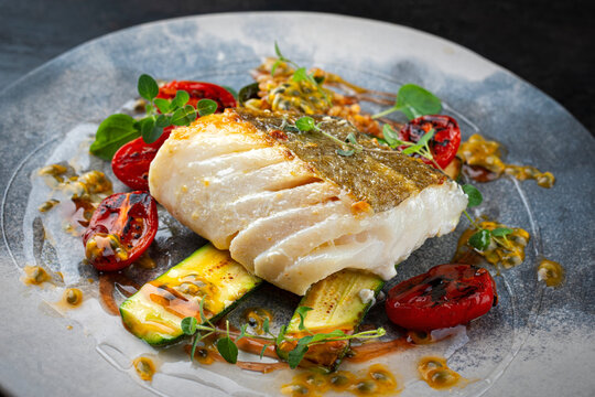 Fried skrei cod white sea fish filet with green vegetable and tomato, rice passion fruit relish umami sauce  Mediterranean dish recipe served as close-up on a design plate
