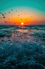 A vibrant close-up captures the dynamic energy of a powerful water splash, frozen in time against the breathtaking backdrop of a vivid sunset or sunrise. The brilliant golden-orange sun casts a warm, 