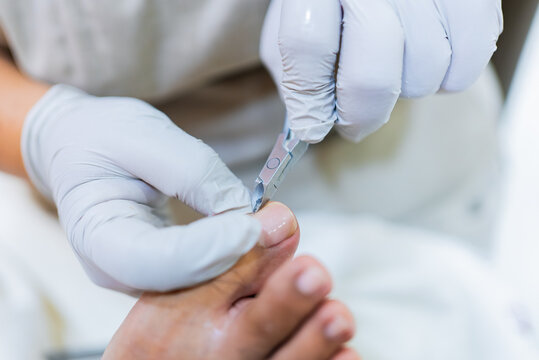 Hand in gloves performing pedicure trimming toenail for foot care