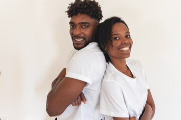 Smiling African American couple standing back to back against a white wall, dressed casually in white T-shirts, showing confidence, happiness, equality, and a strong, supportive relationship
