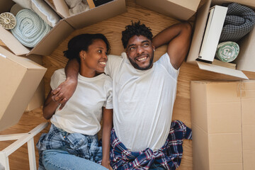 Happy couple lying on the floor surrounded by moving boxes, relaxing after unpacking in their new home and daydreaming about their future together