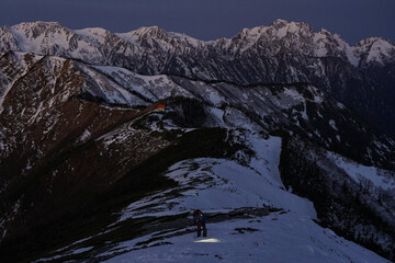 満月の夜明けに初冬の爺ヶ岳を登る人