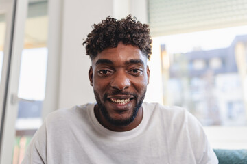 Portrait of a smiling young Black man at home, looking directly at the camera in a relaxed and friendly atmosphere with natural daylight