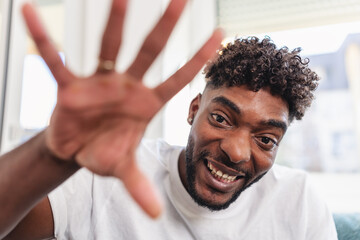 Cheerful man smiling and playfully reaching toward the camera indoors. Casual setting with natural light, expressing friendliness, joy, and positive energy in a relaxed, candid moment