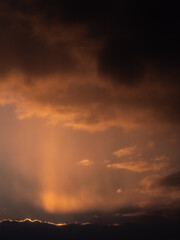 Golden sunset rays shining through thick dark clouds, creating a dramatic and moody evening sky with warm orange tones