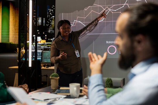 Diverse company work team reviewing budgeting situation on a projector, organizing a briefing meeting late at night to share ideas and details for the strategy. Making decisions for a project.