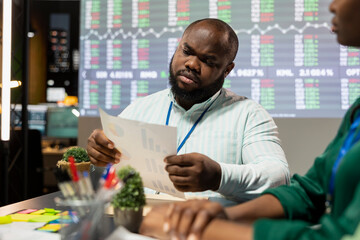 Black general director looking into statistics and reports to detect any obstacles within the project structure, preparing solutions to ensure workflow. Eliminate challenges in night meeting.