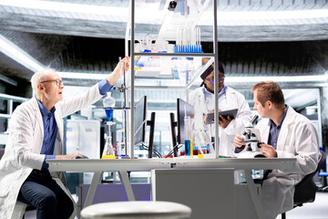 Employees group studying sample tray under the microscope for research study in a lab, sliding the...