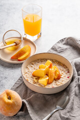 Oatmeal with peaches and nuts  in a bowl on a light background with honey