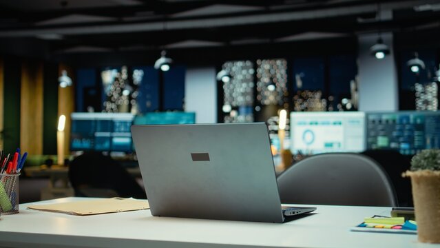 Modern empty office glows with the light of performance metrics and forecasting graphs. Corporate space equipped with technology and computers reflects administration of enterprise objectives.