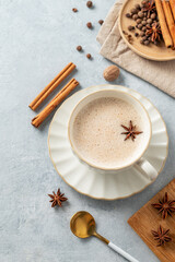 Traditional Indian masala chai tea with milk and spices in a white cup on a light blue background